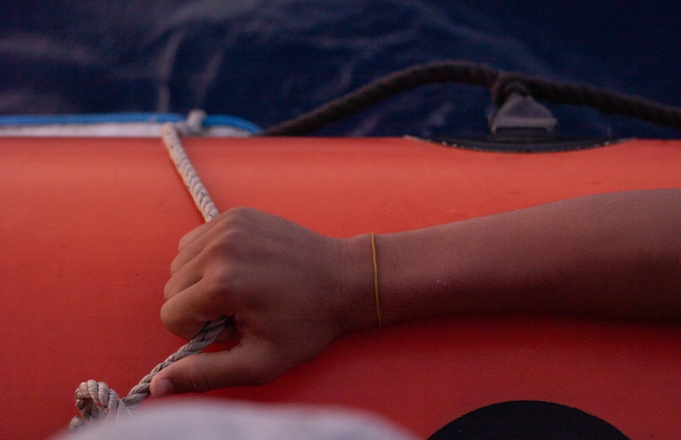 Een hand houdt het touw op een rode reddingsboot vast. 